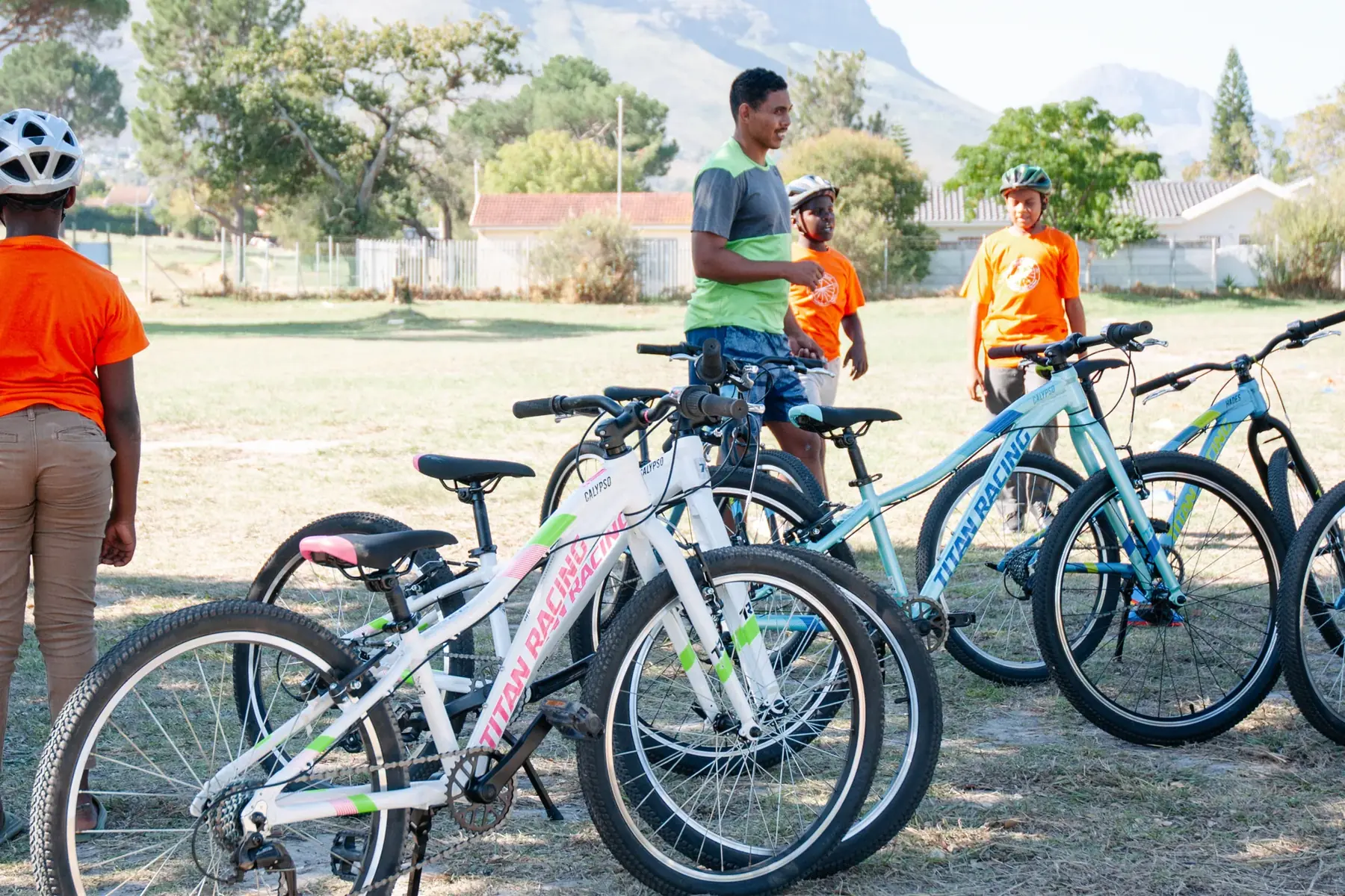 Bicycles parked on a field with young people and mountains behind